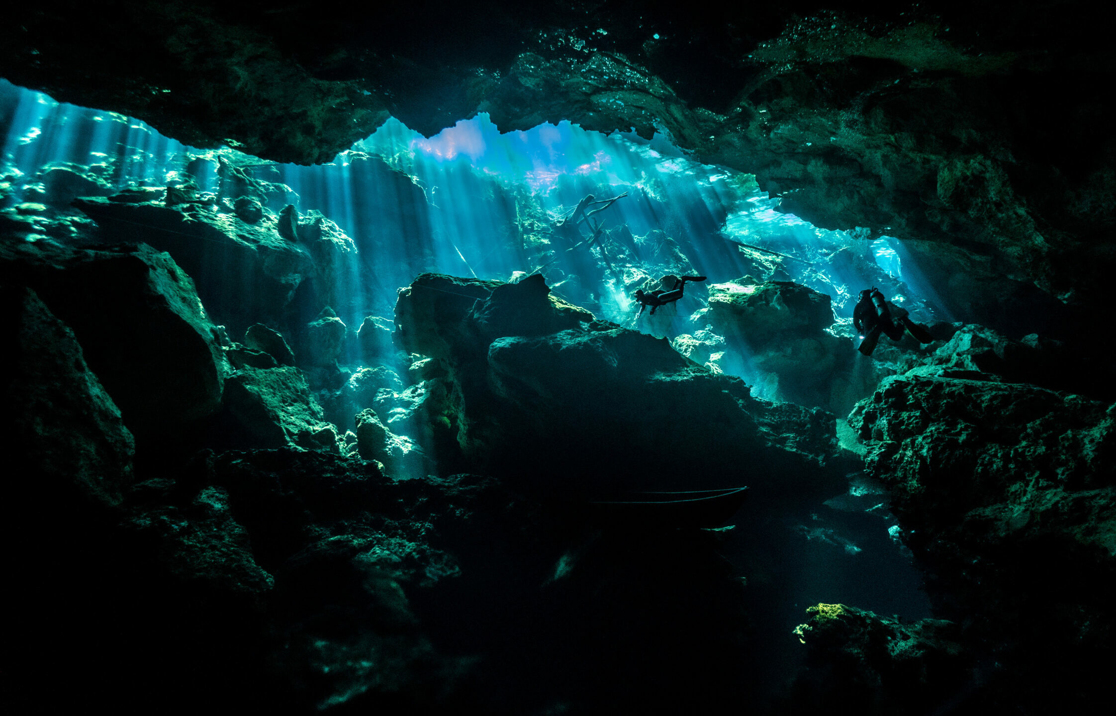 Scuba divers explore the underwater caverns of Chac Mool cenote illuminated by celestial light beams.