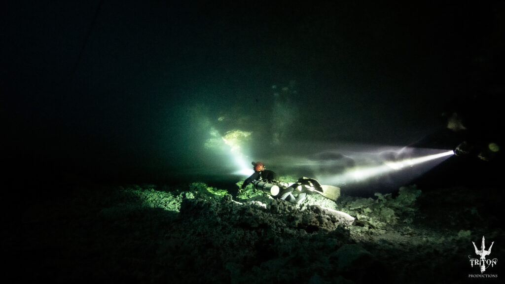 Diver shines a flashlight across the rocky bottom of Chac Mool cenote, creating a dramatic contrast of light and dark.